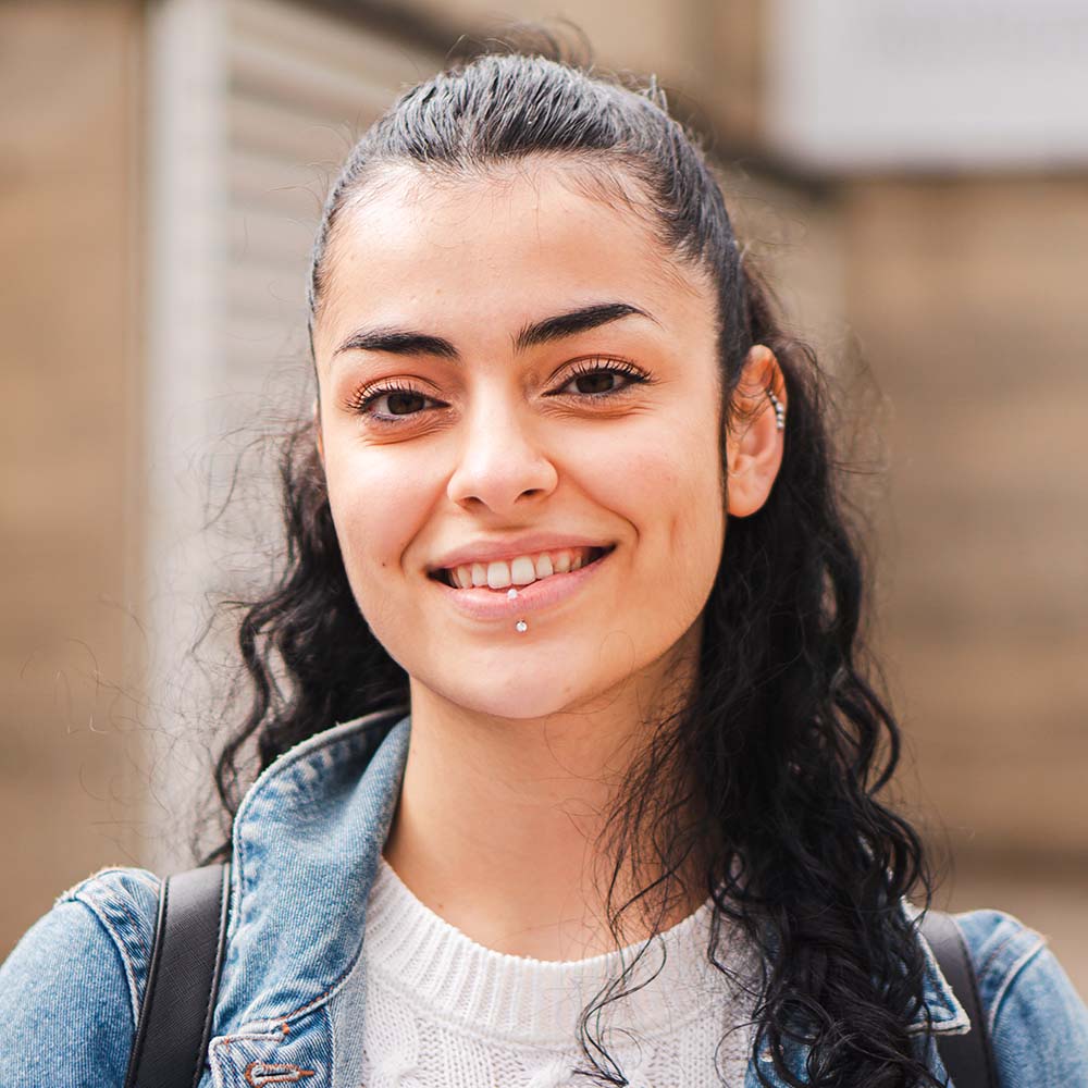 Pretty hispanic female student smiling and looking at camera in the high school. Head shot portrait of latin teenager girl standing outdoors at the university campus. Education concept. High quality photo